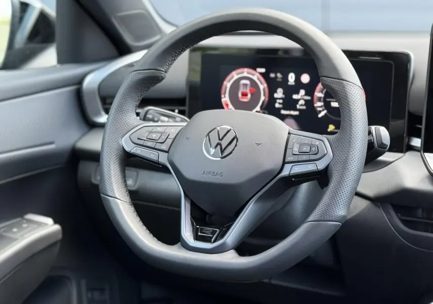 Gros plan sur le volant sport en cuir noir du Volkswagen T-Roc 2026 avec tableau de bord numérique en arrière-plan.