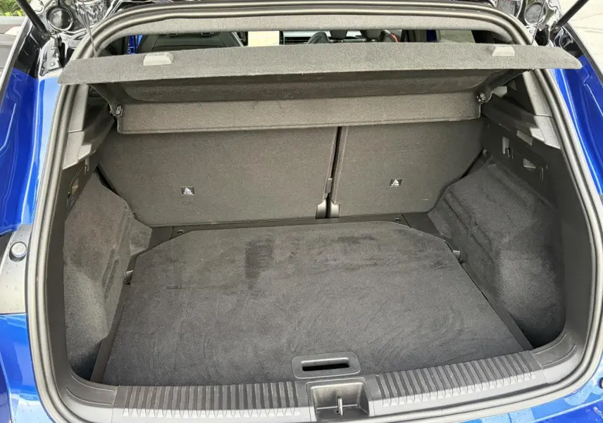 Coffre ouvert vu de l'arrière d'un Renault Austral bleu Iron avec intérieur de coffre noir et cache-bagages déployé.