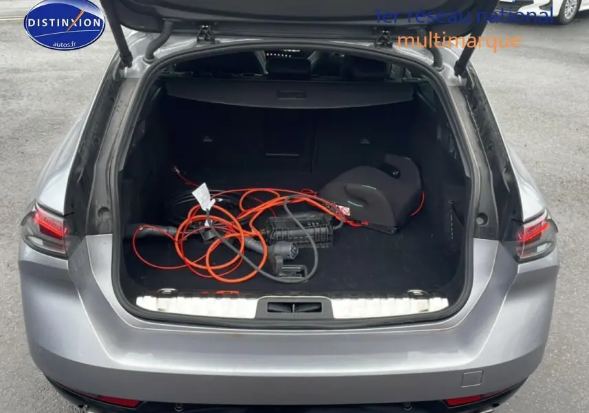 Coffre ouvert vu de l’arrière d’une Peugeot 508 SW gris artense avec câble de recharge hybride visible.