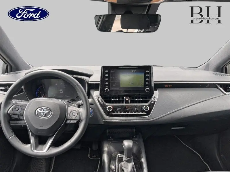 Vue intérieure frontale du tableau de bord et volant cuir noir de la Toyota Corolla 184h Dynamic Business 2022 avec écran tactile central.