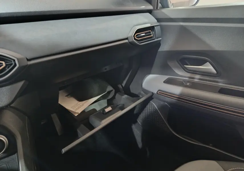 Vue intérieure côté passager de la Dacia Sandero Extreme+ 2024, tableau de bord noir avec boîte à gants ouverte.