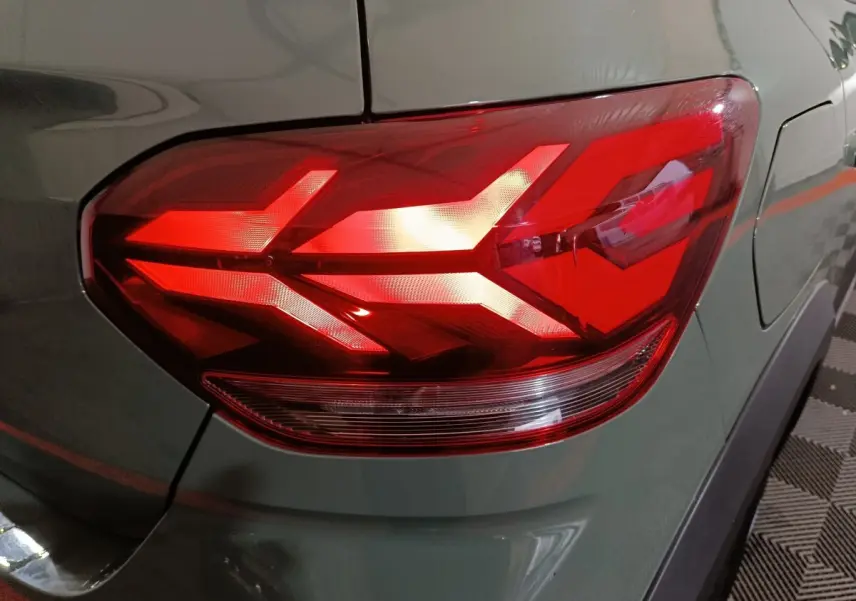 Gros plan sur le feu arrière droit rouge vif d'une Dacia Sandero Extreme+ vert 2024, avec carrosserie et pare-chocs visibles.