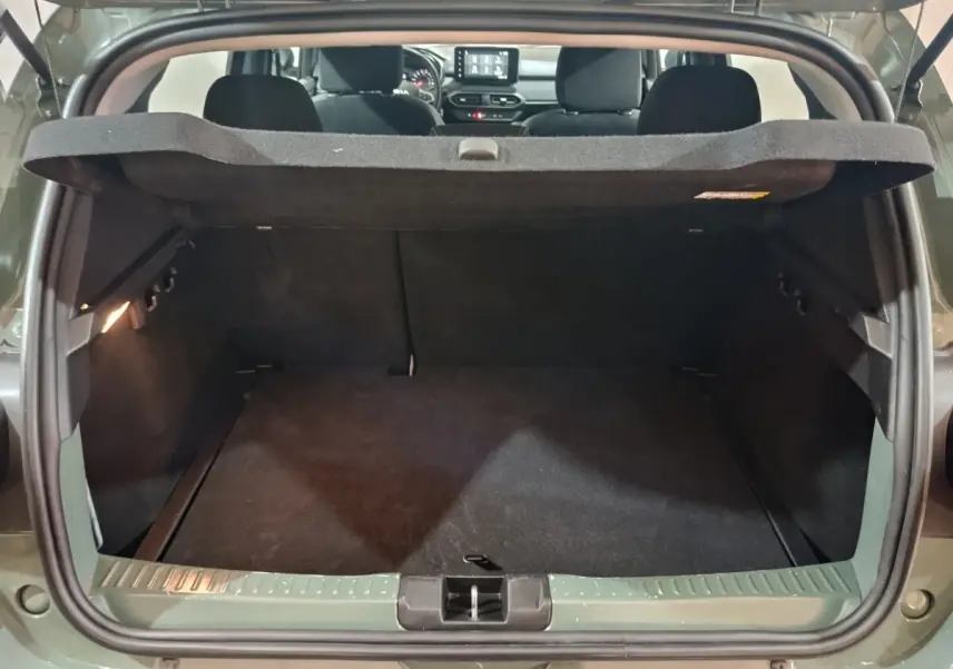 Coffre ouvert vu de l'arrière d'une Dacia Sandero Extreme+ TCe 110 vert, intérieur noir et tablette de coffre relevée.