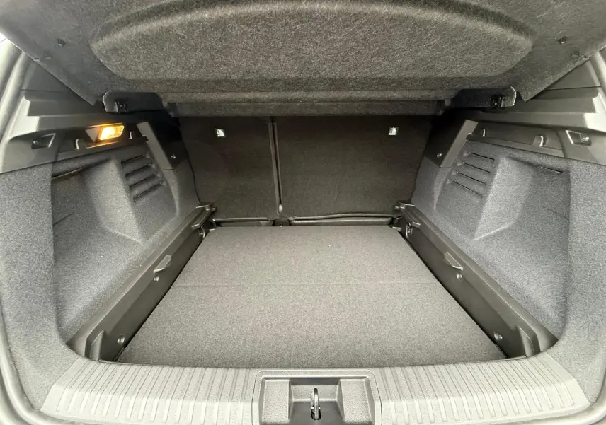 Coffre ouvert vu de l'arrière, intérieur spacieux et gris foncé, éclairage latéral à gauche visible.