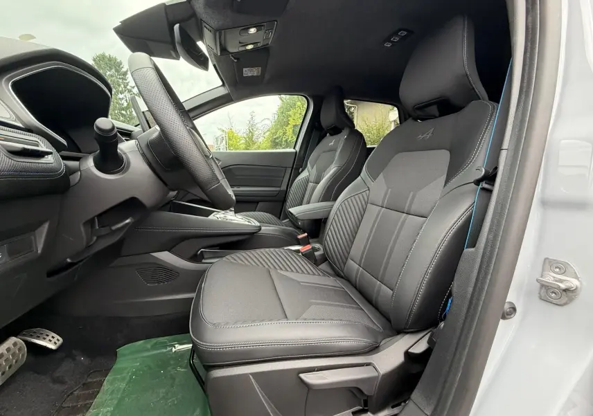 Vue intérieure côté conducteur de la Renault Symbioz gris rafale, sièges sport noirs avec surpiqûres bleues et volant cuir.