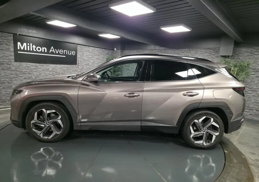 Vue de profil côté gauche d'un Hyundai Tucson gris métallisé avec jantes alliage et vitres teintées dans un showroom.