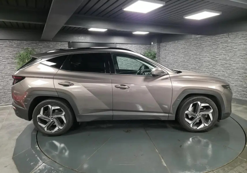Vue latérale droite d'un Hyundai Tucson gris métallisé avec jantes alliage et vitres teintées en intérieur fermé.