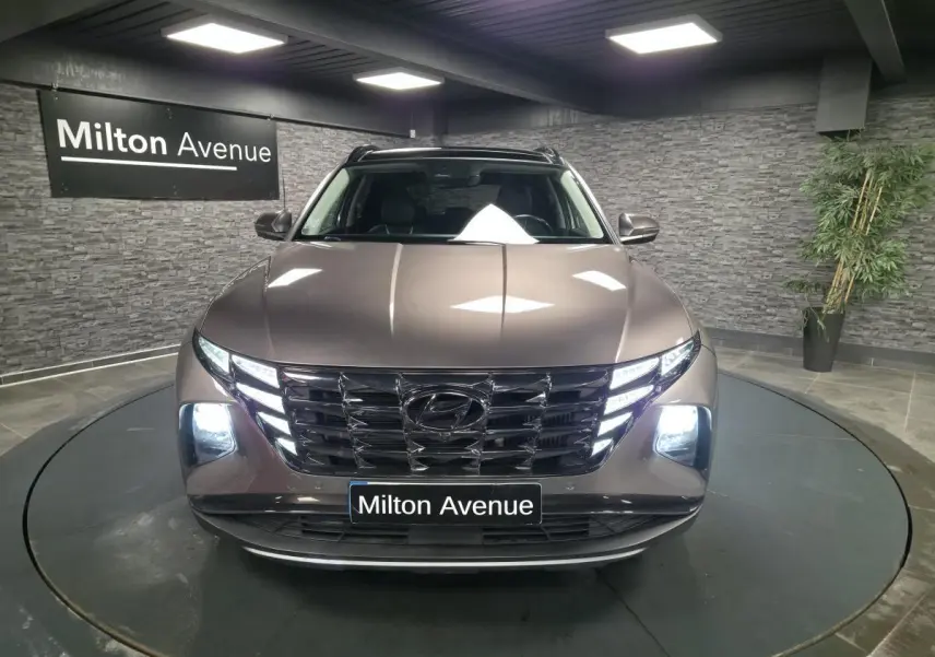 Vue avant d’un Hyundai Tucson gris métallisé avec calandre chromée et feux LED allumés en showroom.