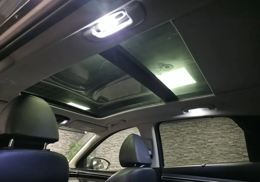 Vue intérieure du toit ouvrant panoramique et des sièges avant en cuir noir du Hyundai Tucson gris, avec éclairage intérieur allumé.