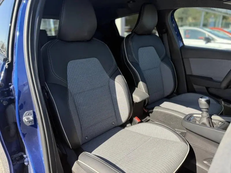 Vue intérieure côté gauche de la Renault Clio 2025 Bleu Iron, montrant les sièges avant et la boîte manuelle.