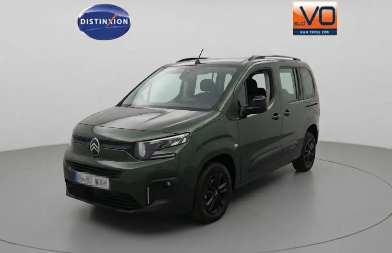Vue 3/4 avant d'un Citroën Berlingo vert avec barres de toit et jantes noires dans un studio blanc.