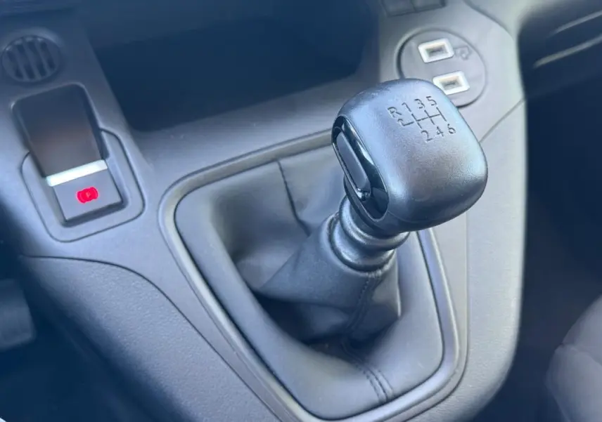 Gros plan sur le levier de vitesse manuel noir du Citroën Berlingo vert, avec frein à main électrique visible à gauche.
