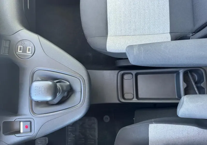 Vue intérieure centrée sur la console centrale et levier de vitesse manuel du Citroën Berlingo 2024, sièges gris et noirs.