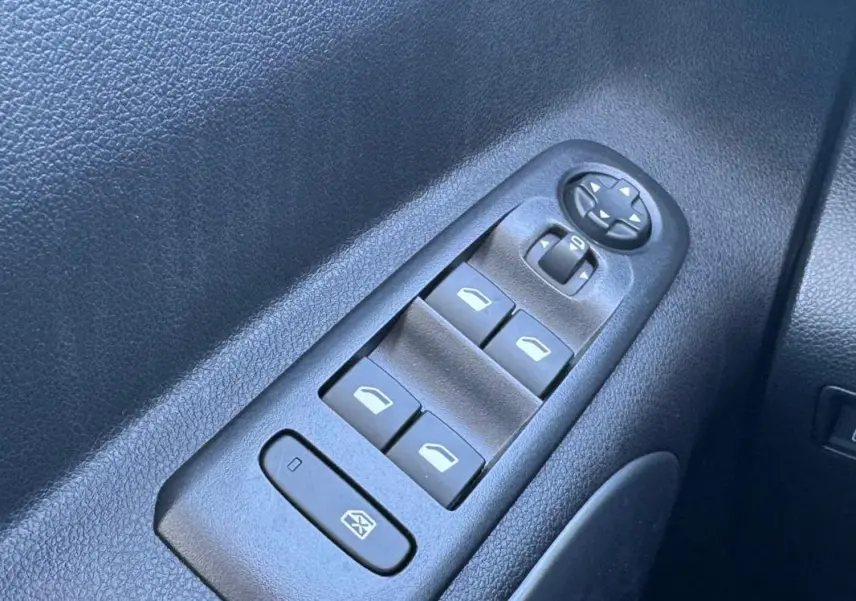 Gros plan sur les commandes des vitres électriques et des rétroviseurs côté conducteur d’un Citroën Berlingo vert 2024.