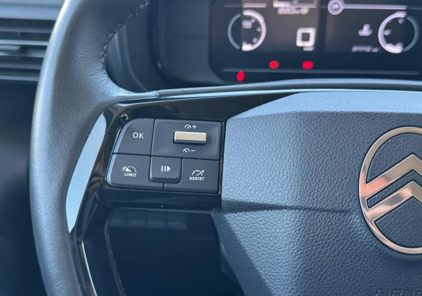 Gros plan sur le volant noir du Citroën Berlingo vert 2024, montrant les commandes de régulateur et limiteur de vitesse.