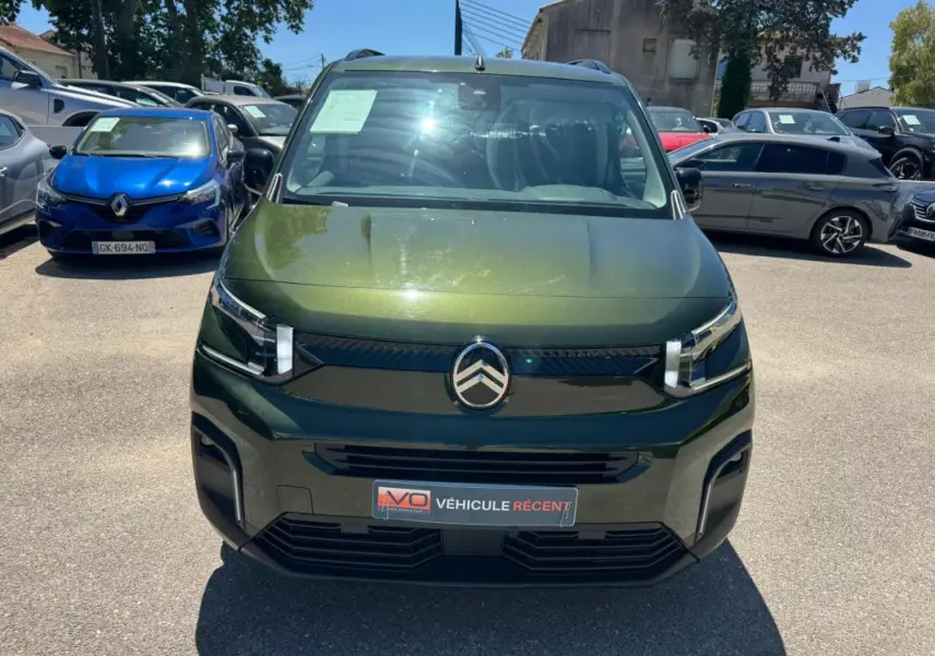 Vue avant d'un Citroën Berlingo vert métallisé avec barres de toit, sur un parking en plein jour.