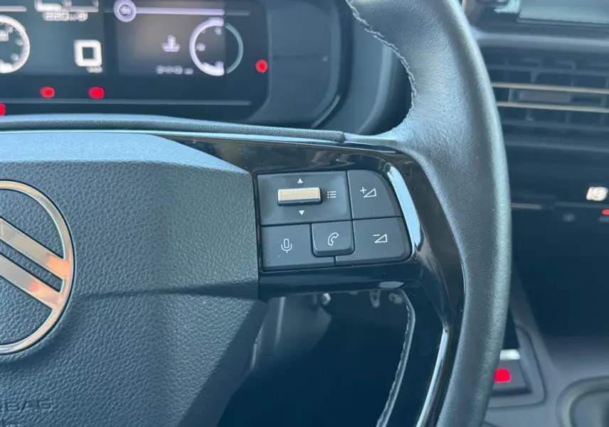 Vue rapprochée du volant noir du Citroën Berlingo vert 2024, avec commandes audio et téléphone intégrées.