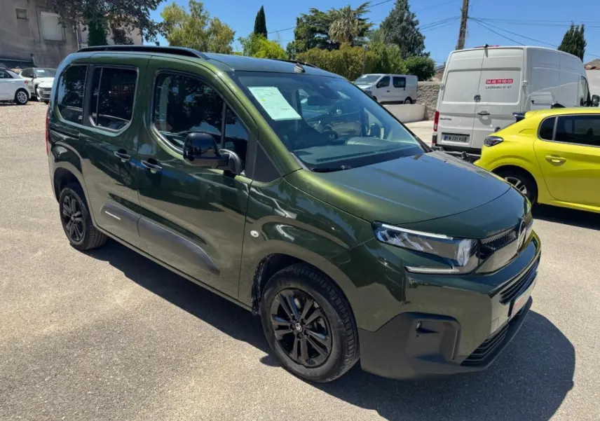 Vue 3/4 avant droit d'un Citroën Berlingo vert 2024 avec barres de toit et jantes noires.