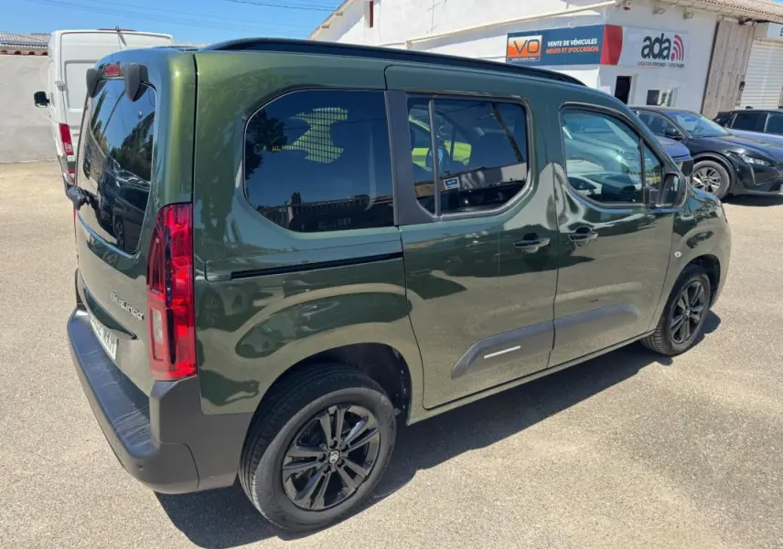 Vue 3/4 arrière droite d'un Citroën Berlingo vert 2024 avec barres de toit et vitres teintées.
