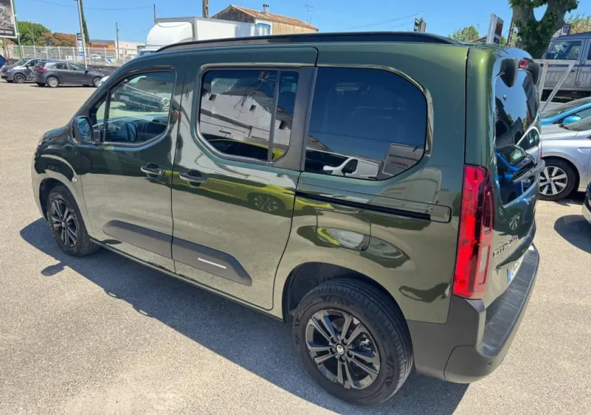 Vue 3/4 arrière droite d'un Citroën Berlingo vert 2024 avec barres de toit et vitres teintées.