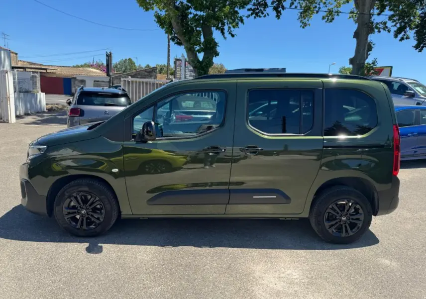 Vue de profil côté gauche d'un Citroën Berlingo vert 2024 avec barres de toit et jantes noires.