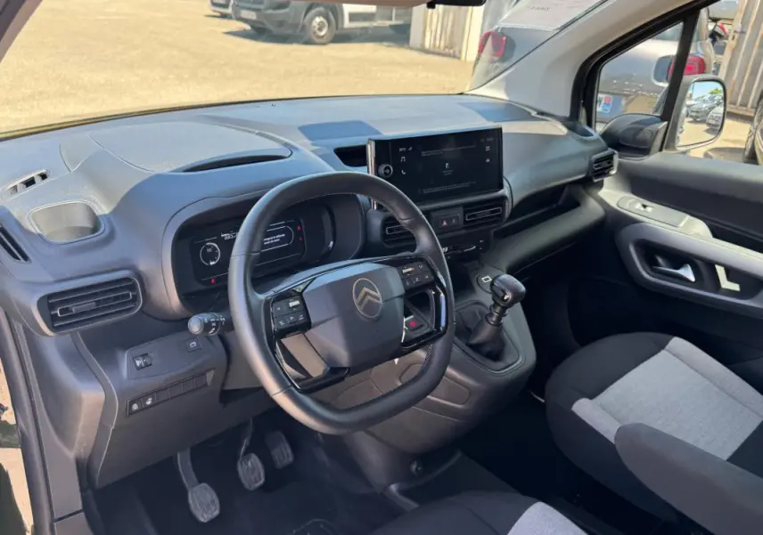 Vue intérieure côté conducteur du Citroën Berlingo 2024, tableau de bord noir avec écran central et volant multifonction.