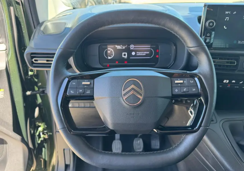 Vue rapprochée du volant noir du Citroën Berlingo vert 2024, avec commandes intégrées et tableau de bord numérique.