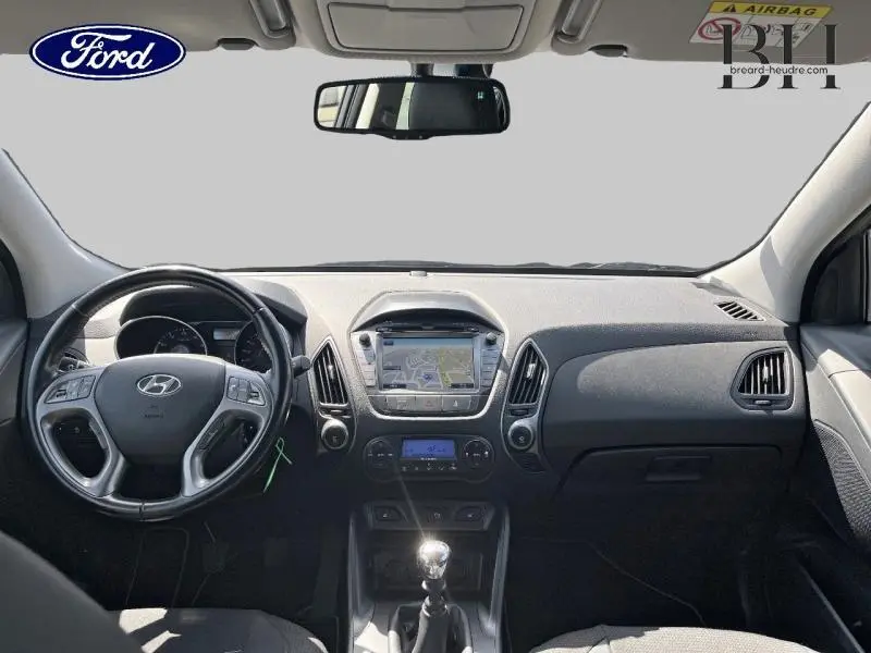 Vue intérieure avant du tableau de bord et volant cuir noir d'un Hyundai ix35 gris acier avec boîte manuelle et écran central tactile.