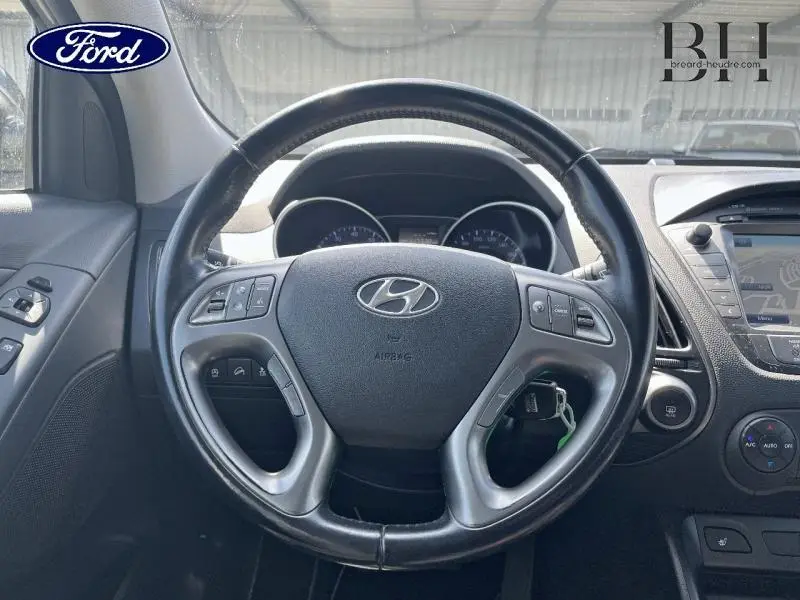 Vue centrée sur le volant cuir d'une Hyundai ix35 2014, avec tableau de bord et commandes visibles en arrière-plan.