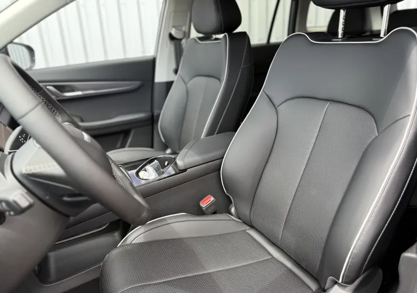 Vue intérieure côté conducteur du JAECOO J5 2026, sièges en cuir noir avec surpiqûres blanches et console centrale visible.