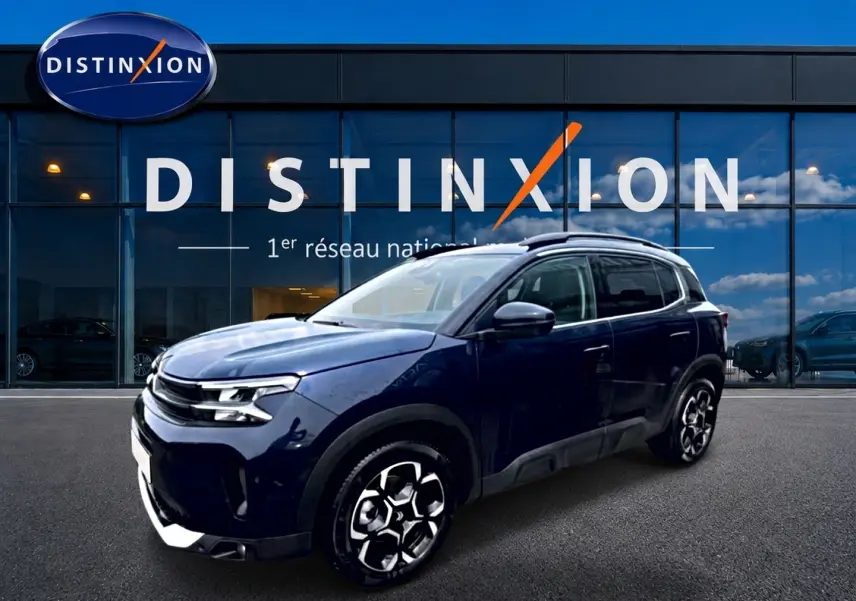 Vue 3/4 avant droite d'un Citroën C5 Aircross bleu eclipse avec jantes alu devant une vitrine Distinxion.