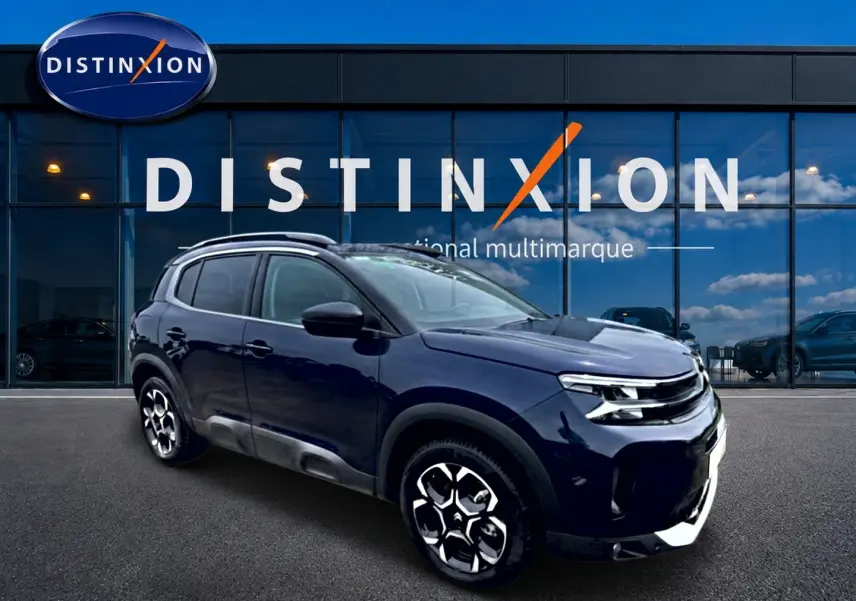 Citroën C5 Aircross bleu eclipse en 3/4 avant droit, avec jantes alu et barres de toit visibles devant vitrine Distinxion.