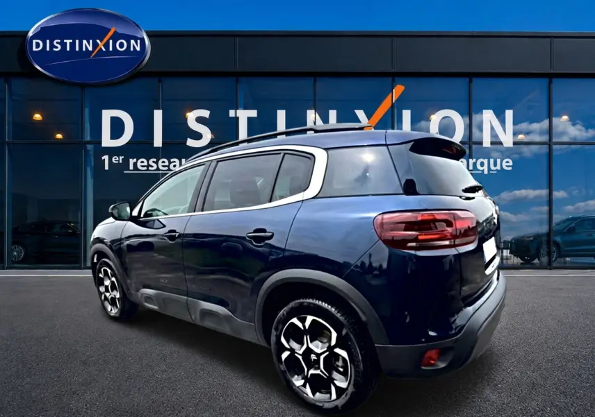 Vue 3/4 arrière droite d'un Citroën C5 Aircross bleu eclipse avec jantes alu et barres de toit visibles.