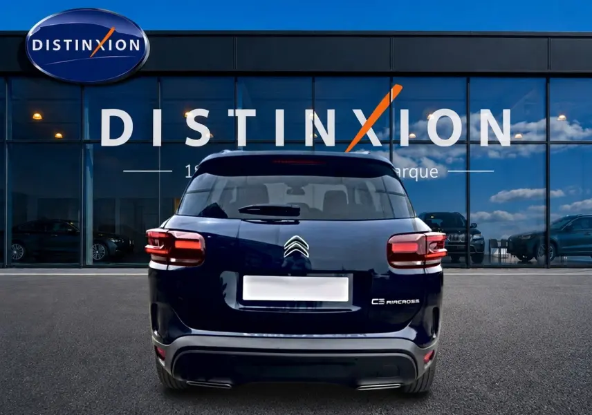 Vue arrière d’un Citroën C5 Aircross bleu eclipse garé devant une vitrine avec logo Distinxion.