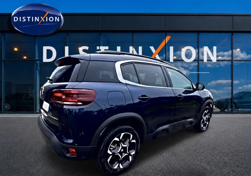 Vue 3/4 arrière droite d’un Citroën C5 Aircross bleu eclipse avec jantes alu et barres de toit visibles.
