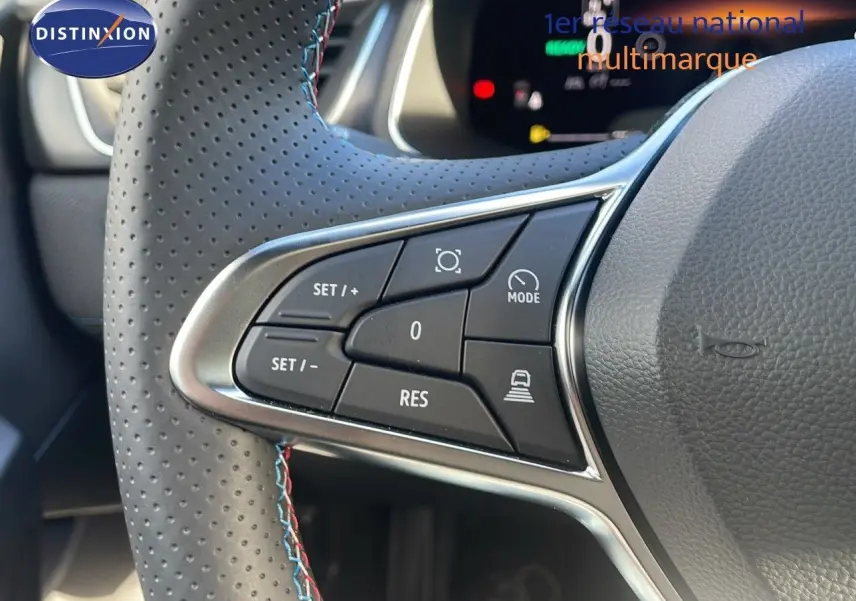 Gros plan sur les commandes au volant perforé avec surpiqûres bleu et rouge du Renault Captur gris Rafale 2025.