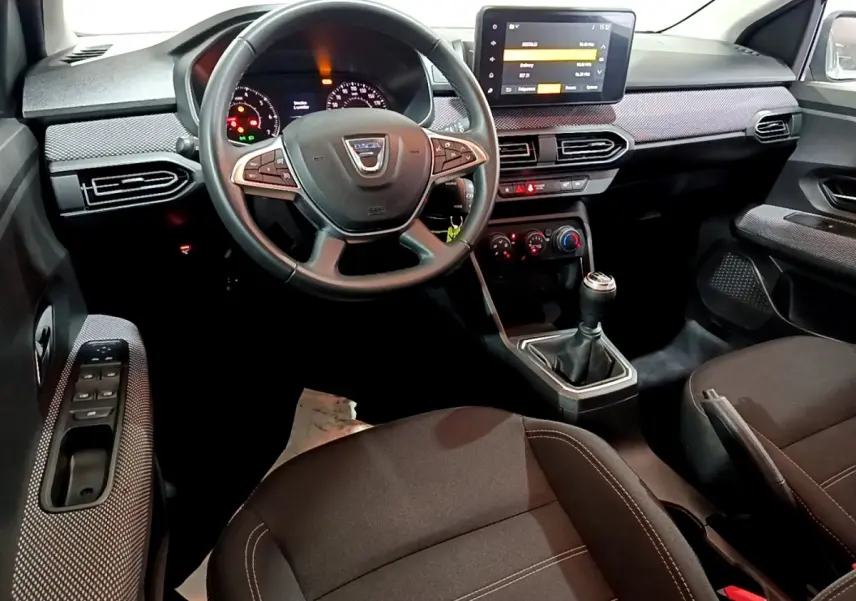 Vue intérieure côté conducteur de la Dacia Sandero 2022, volant cuir multifonctions et écran tactile central visible.