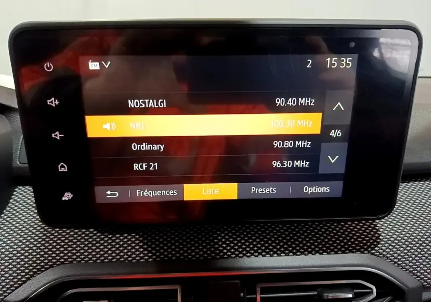 Écran tactile central affichant la liste des radios dans l’habitacle d’une Dacia Sandero blanche vue de face.