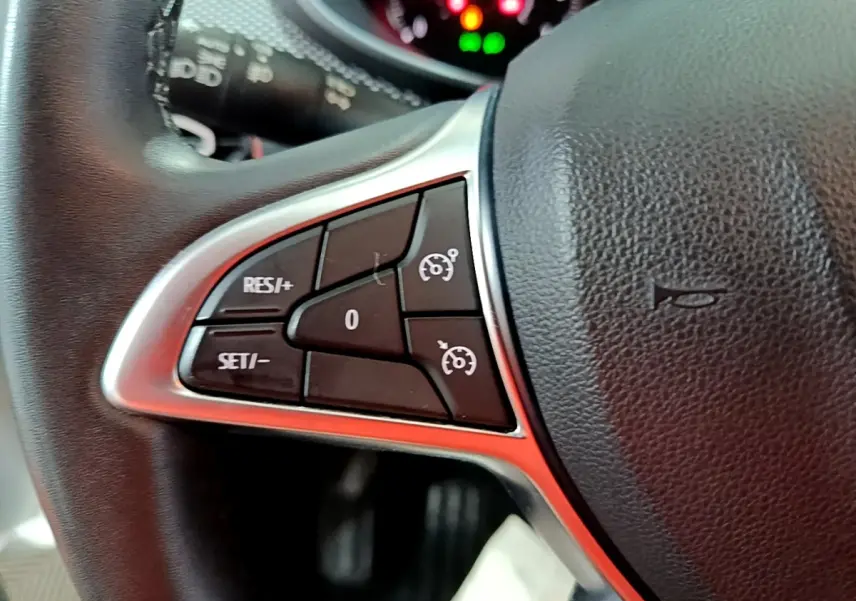 Gros plan sur le côté gauche du volant cuir synthétique noir du Dacia Sandero blanc, avec commandes de régulateur de vitesse.