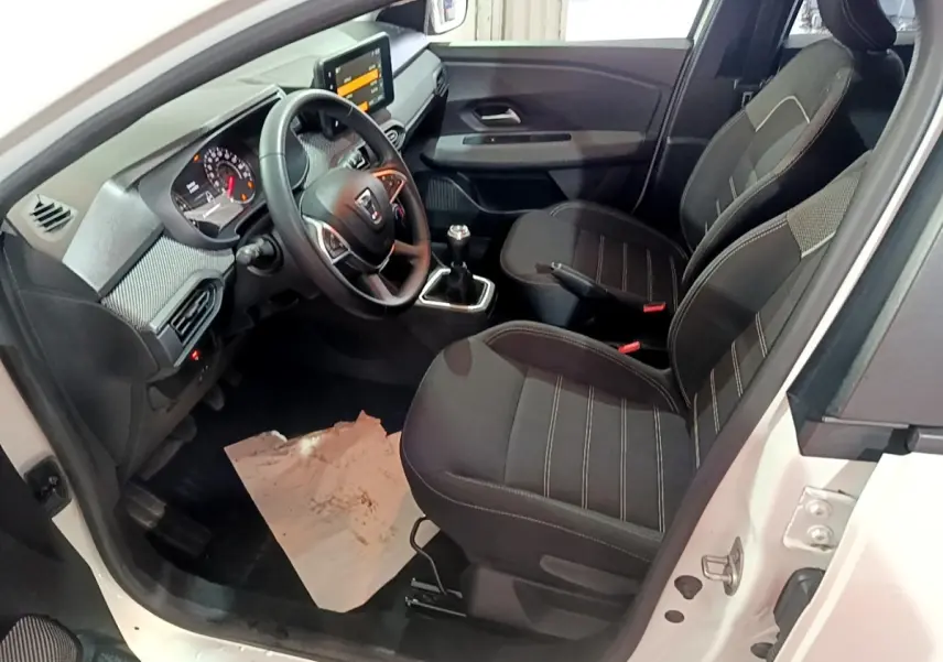Vue intérieure côté conducteur d'une Dacia Sandero blanc 2022, volant cuir multifonctions et sièges tissu noirs.