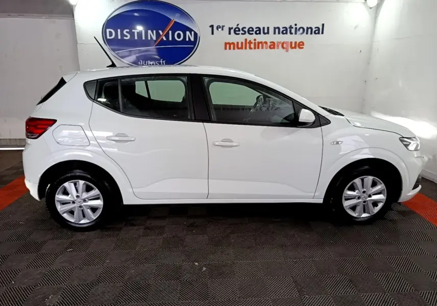 Vue de profil côté gauche d'une Dacia Sandero blanche 2022 dans un garage avec logo Distinxion en arrière-plan.
