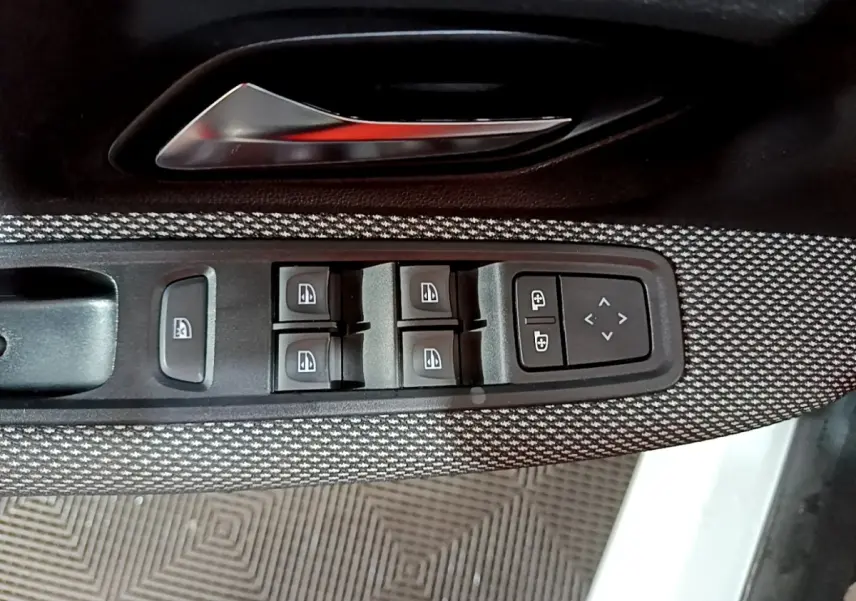 Gros plan sur la commande des vitres électriques et réglages des rétroviseurs côté conducteur d'une Dacia Sandero blanche.