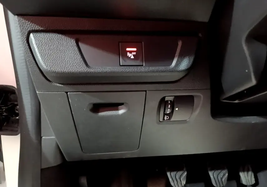 Vue intérieure côté conducteur de la Dacia Sandero blanche, avec commandes d'éclairage et bouton d'aide au stationnement activé.