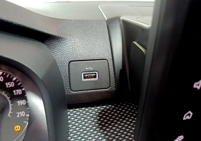 Gros plan intérieur sur la prise USB noire à côté du tableau de bord et du compteur de vitesse partiel de la Dacia Sandero blanche.