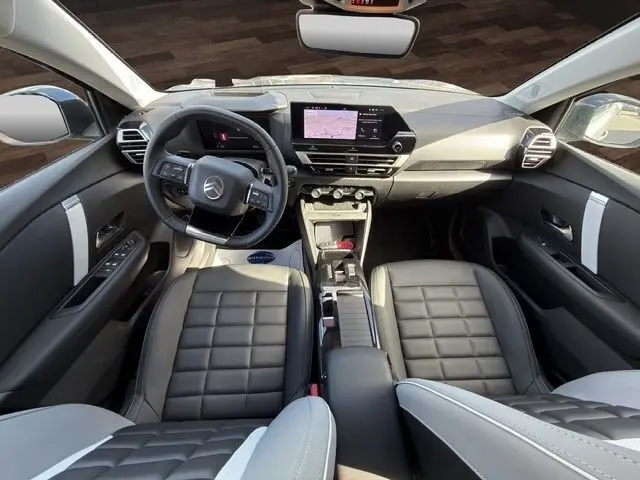 Vue intérieure avant de la Citroën C4 hybride 2025 avec sièges cuir noirs, tableau de bord numérique et écran tactile central.