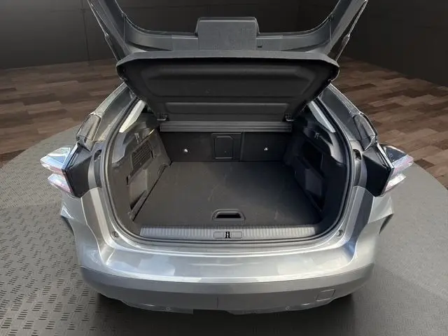 Coffre ouvert vu de l'arrière d'une Citroën C4 hybride gris clair, montrant l'espace de chargement vide.