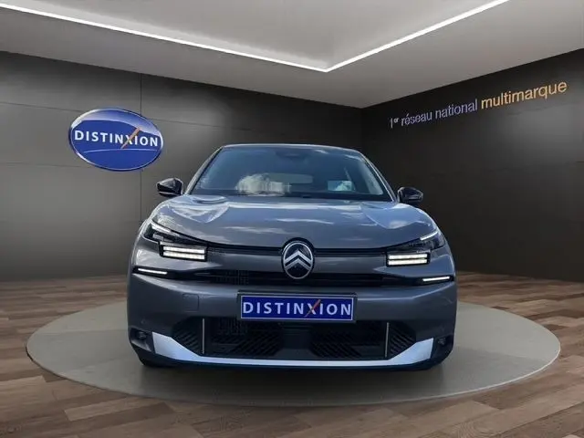 Vue frontale d'une Citroën C4 hybride gris clair avec phares LED et logo distinctif sur fond showroom.