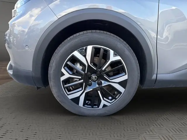 Gros plan sur l'aile avant gauche gris clair d'une Citroën C4 hybride 2025, mettant en valeur la roue et le passage de roue.