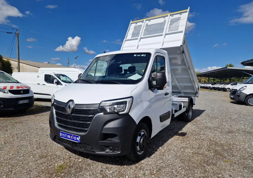 Renault Master Benne blanc en 3/4 avant droit, benne relevée et roues jumelées visibles sous un ciel bleu.