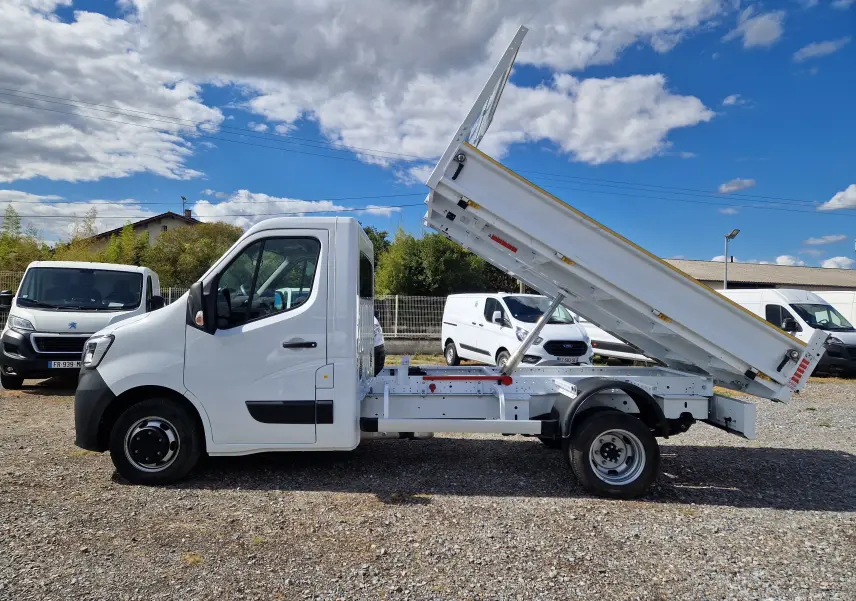Vue latérale droite d’un Renault Master blanc 2024 avec benne basculante relevée et roues jumelées arrière.